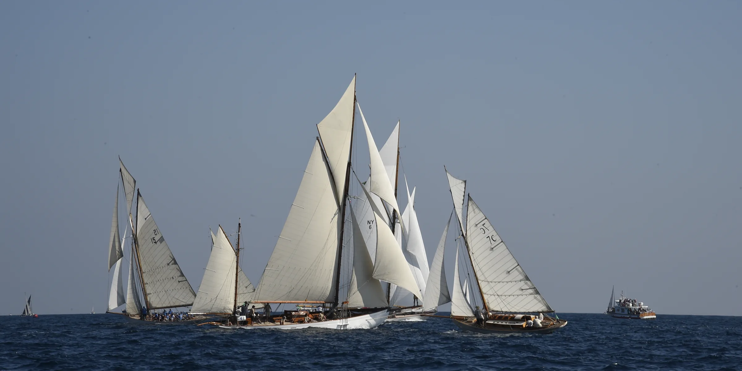 Une dizaine de voiliers classiques au près dans le golfe de Saint-Tropez, sous un ciel dégagé.