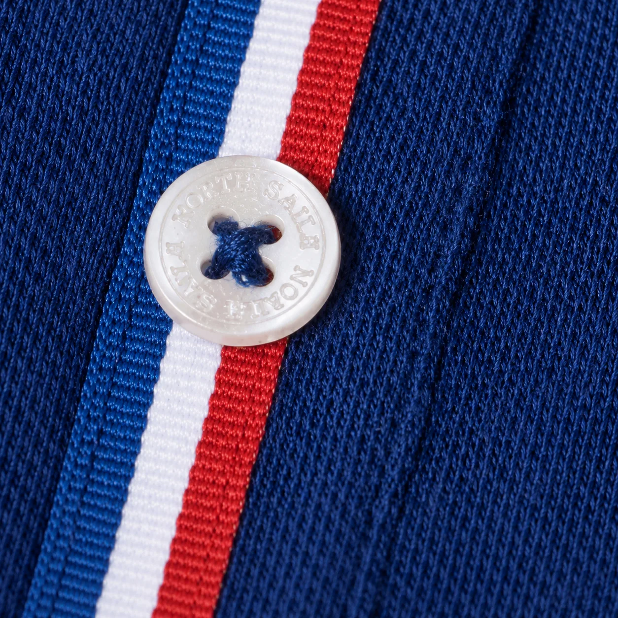Macro d'un bouton de nacre frappé North Sails, cousu sur le galon bleu-blanc-rouge de la patte de boutonnage.