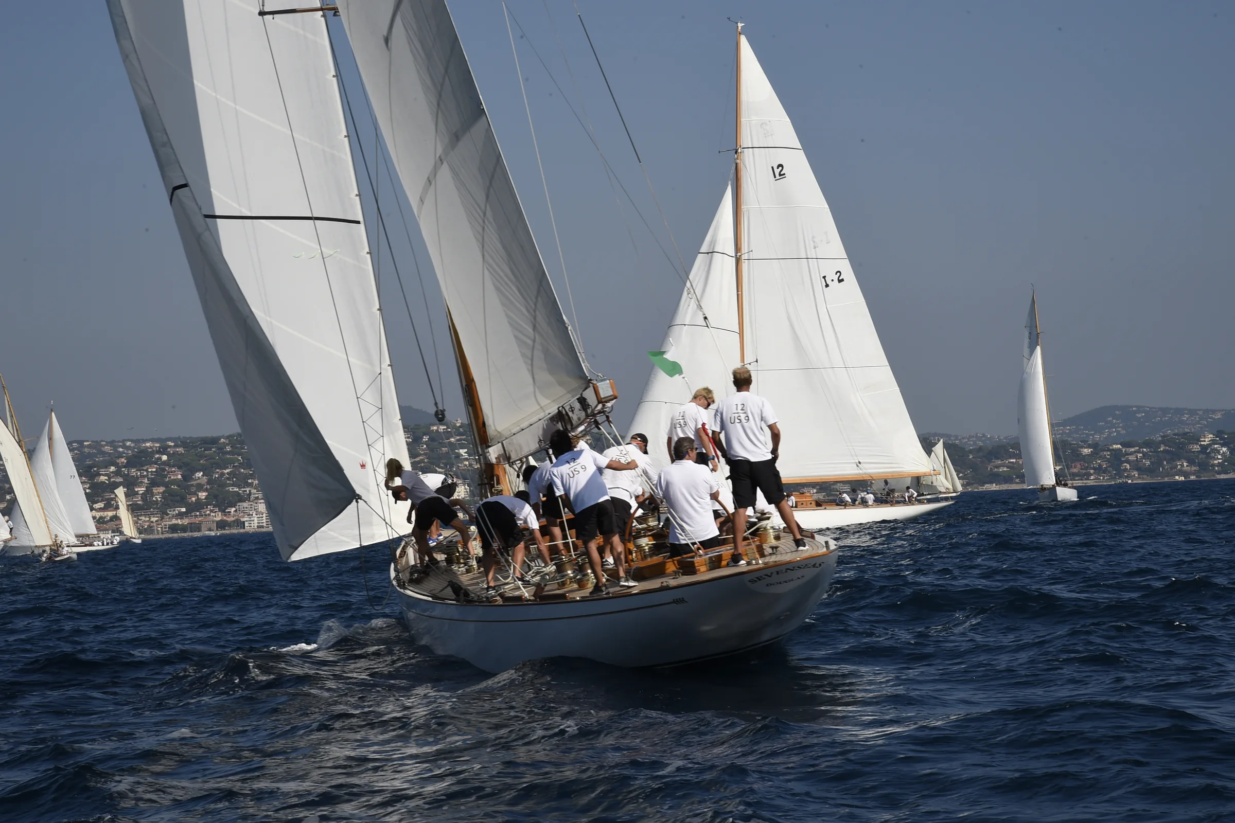 Équipage au rappel sur un voilier classique lancé au près pendant la régate, la flotte en arrière-plan.