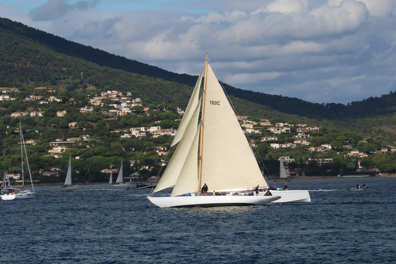 Un voilier classique sous voiles dans le golfe de Saint-Tropez, les collines en arrière-plan.