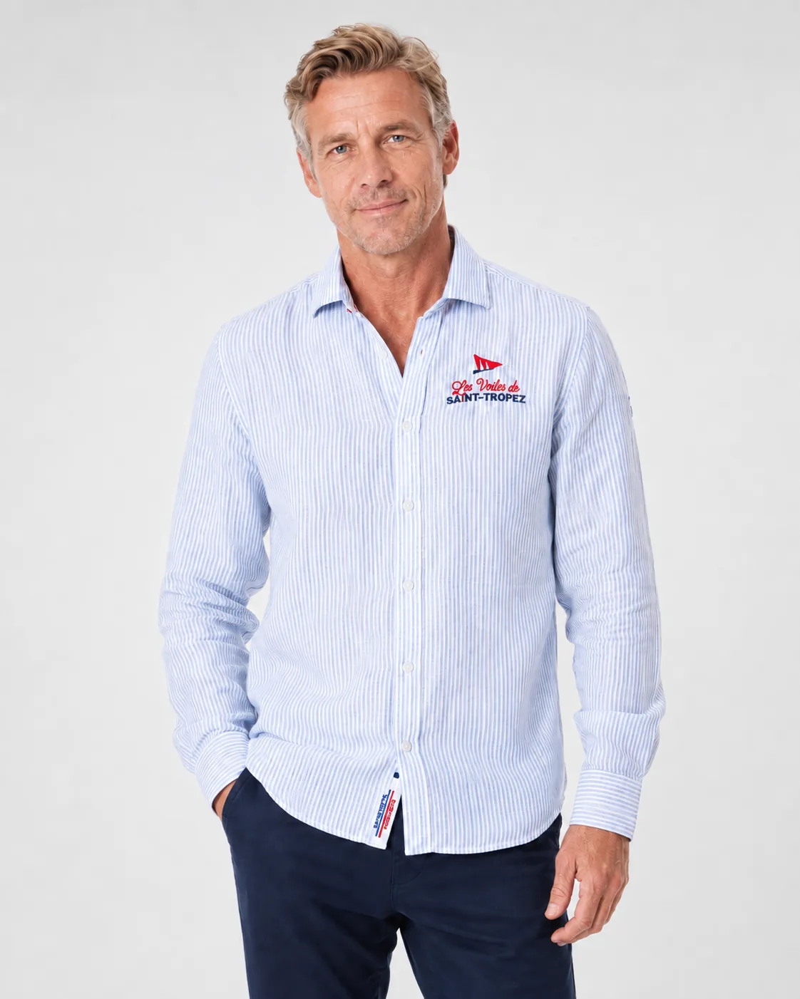 Chemise Lin 26 à fine rayure bleu ciel portée de face : col italien ouvert et broderie du fanion Les Voiles de Saint-Tropez sur la poitrine.