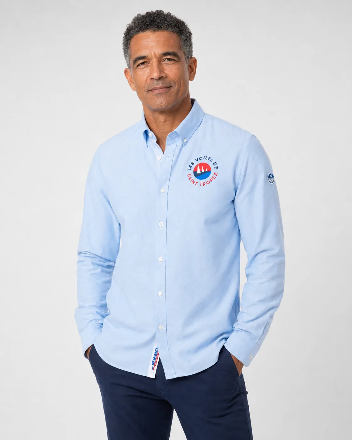Chemise Oxford 26 bleu ciel portée de face : col boutonné et écusson rond Les Voiles de Saint-Tropez sur la poitrine.