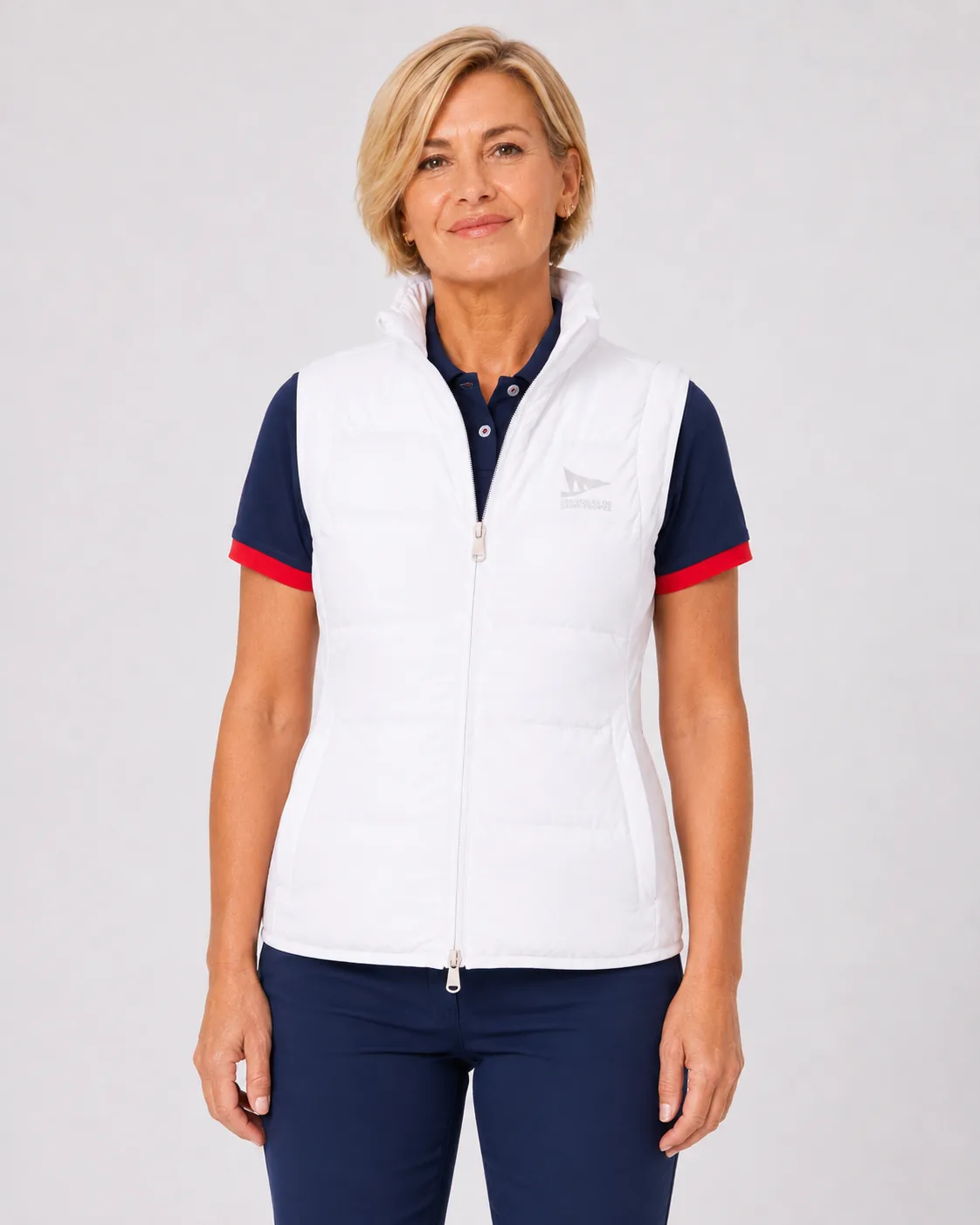 Gilet Sans Manches 26 blanc écru porté sur un polo marine : matelassage soudé au laser, col montant, fermeture zippée intégrale et logo ton sur ton sur la poitrine.