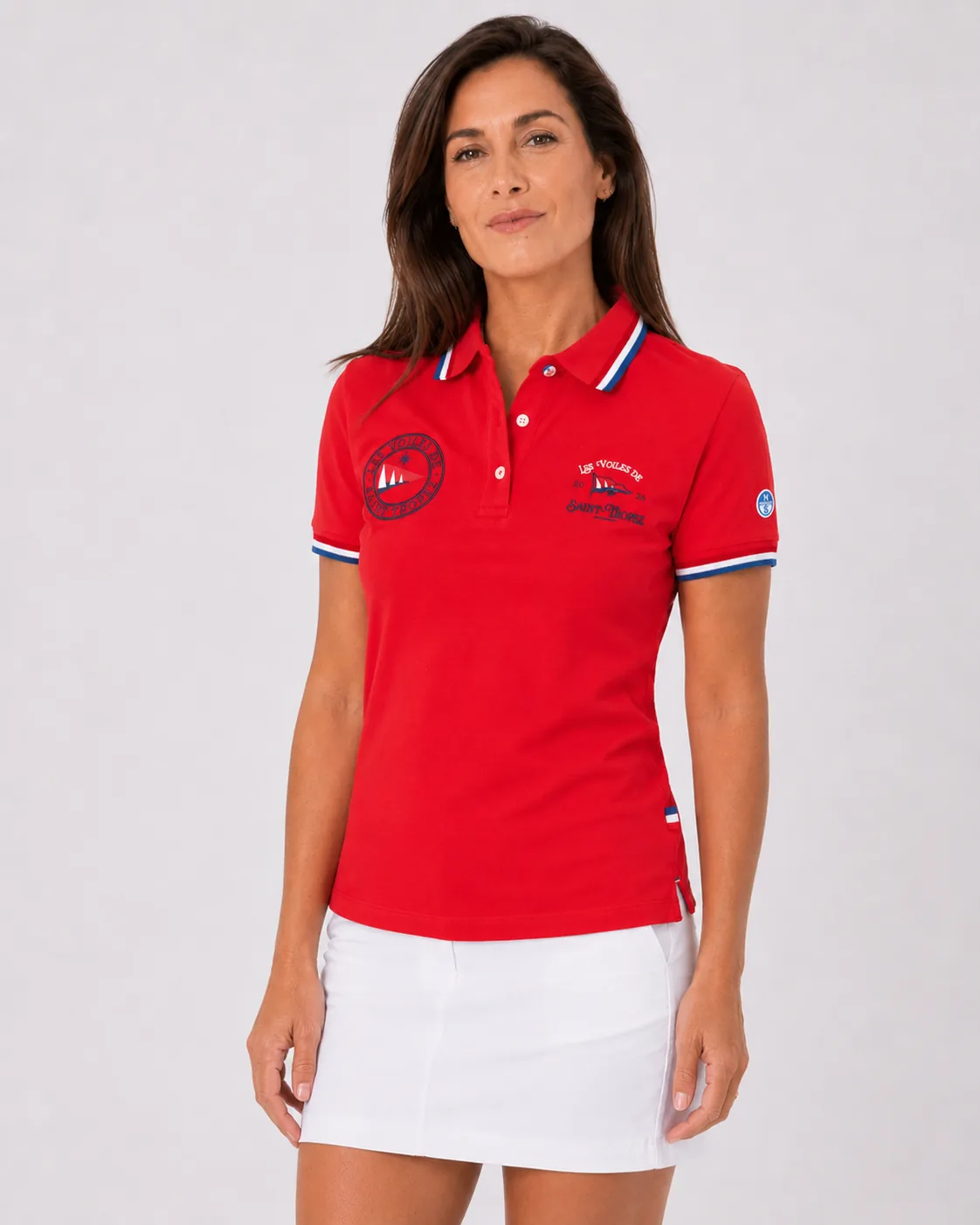 Polo Classique 26 rose bougainvillier porté de face : écusson rond à gauche, mention Les Voiles de Saint-Tropez 2026 à droite, galon tricolore au col et aux poignets, écusson North Sails à la manche.