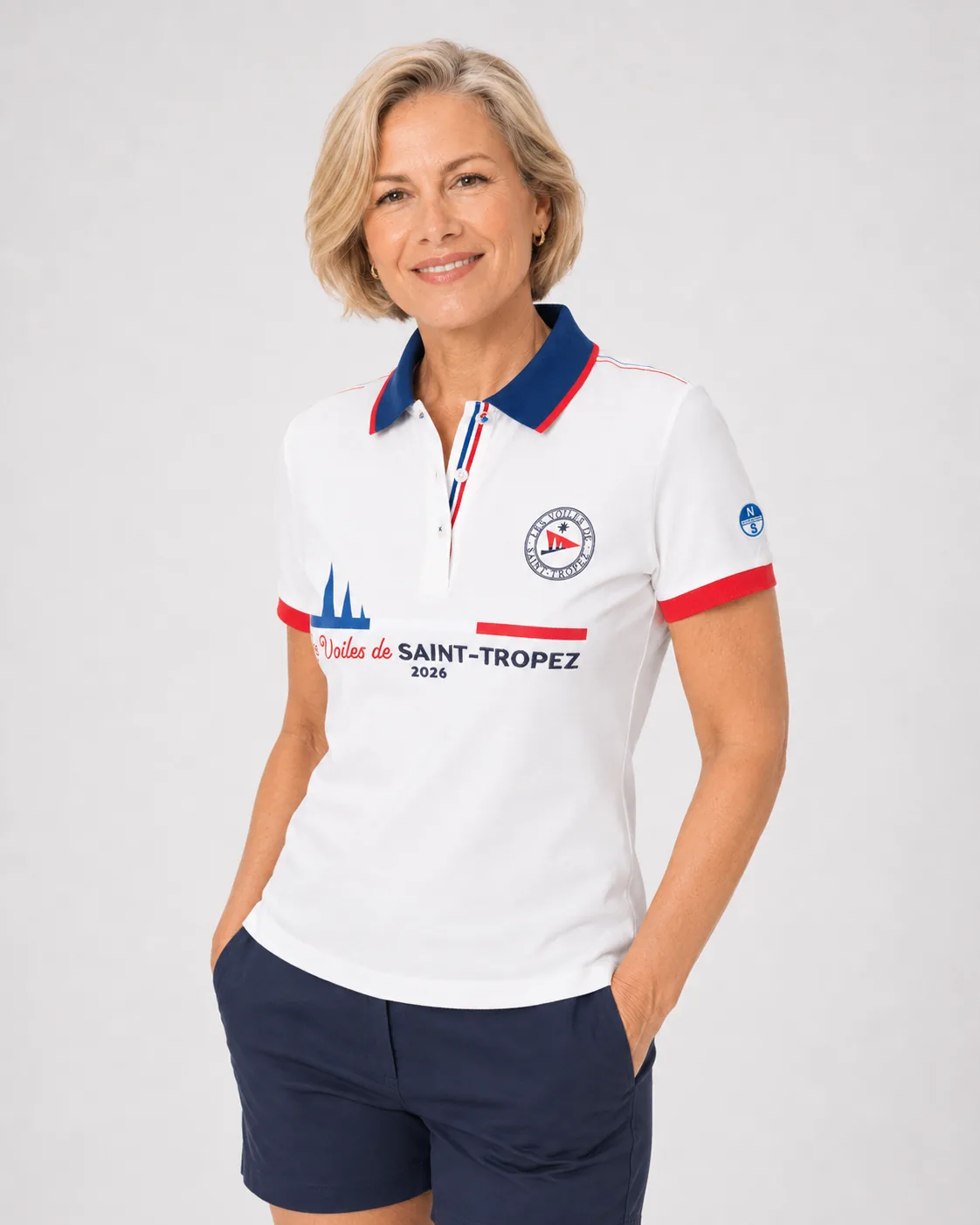Polo Édition Limitée 26 blanc écru porté de face : col marine à liseré rouge, écusson rond, poignets rouges et mention Les Voiles de Saint-Tropez 2026 en grand sur la poitrine.