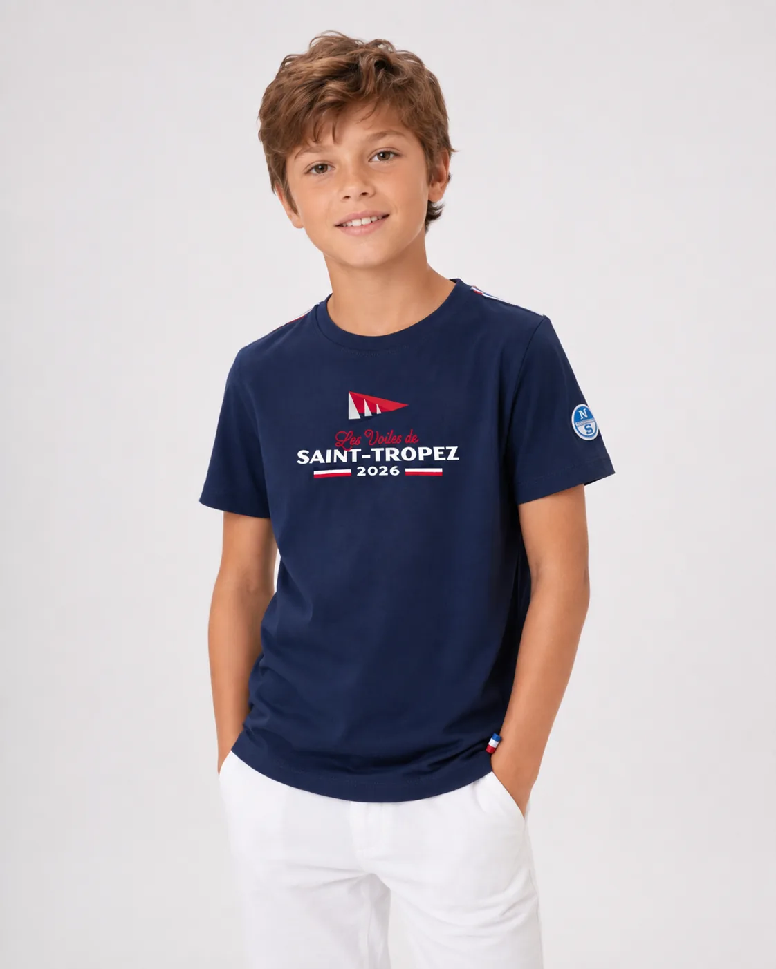 T-Shirt Kids 26 bleu marine porté de face par un enfant : imprimé Les Voiles de Saint-Tropez 2026 sur la poitrine et galon tricolore à l'épaule.
