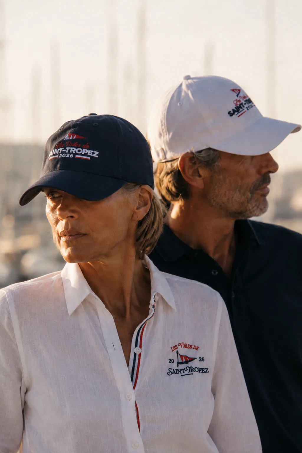 Deux personnes de dos au port, casquettes marine et blanche brodées Les Voiles de Saint-Tropez 2026.