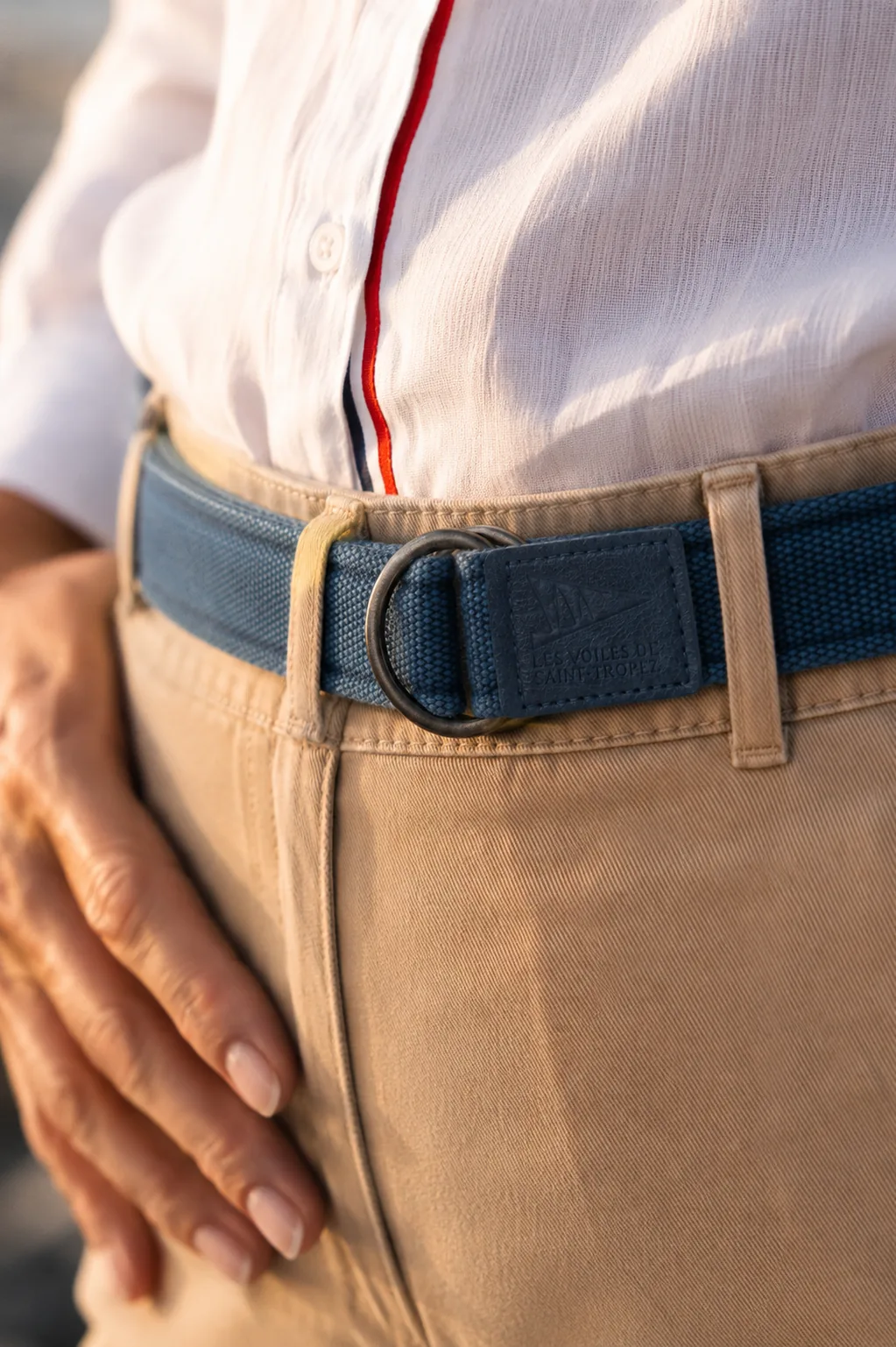 Macro d'une ceinture en toile bleue à double anneau, la patte d'extrémité frappée Les Voiles de Saint-Tropez.