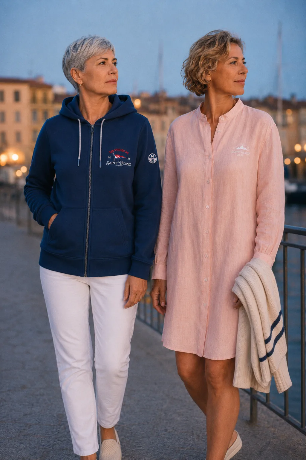 Deux femmes marchent sur le quai à la tombée du jour, en veste zippée marine et robe chemise en lin rose corail.